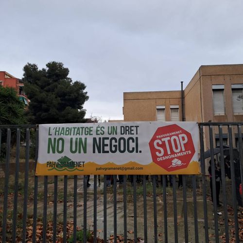 Foto del nou lloc alliberat. Té un pati tancat per una reixa, de la que penja una pancarta de la pahv Gramenet que diu "l'habitatge és un dret, no un negoci"